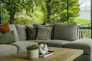 A grey sectional sofa with multiple cushions, a small potted plant, a white ceramic duck, and a wooden coffee table with a book and a plate. - Stunning Lake Views - Queenstown (Queenstown)