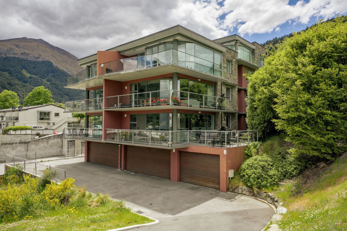 A multi-story building with balconies, a garage, and a mountainous backdrop.