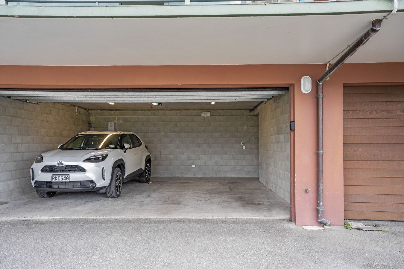 A white SUV parked in a garage with a concrete floor and a brown wall.