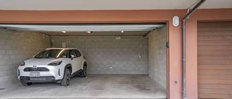 A white SUV parked in a garage with a concrete floor and a brown wall.