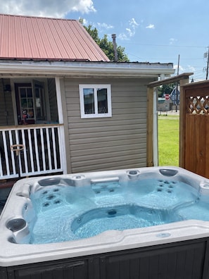 A hot tub in front of a house with a metal roof and a wooden fence.
