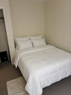 A single-bed room with a white bedspread, a small rug, and a closet to the left.