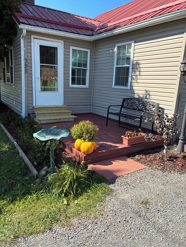 A house with a red roof, a front porch with steps, a bench, and a small garden with a birdbath and potted plants.