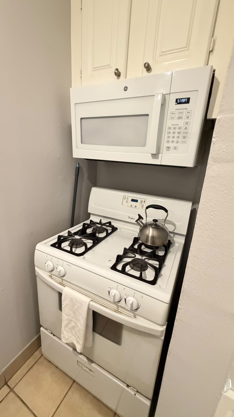 A compact kitchen with a white stove, a microwave above it, and white cabinets.