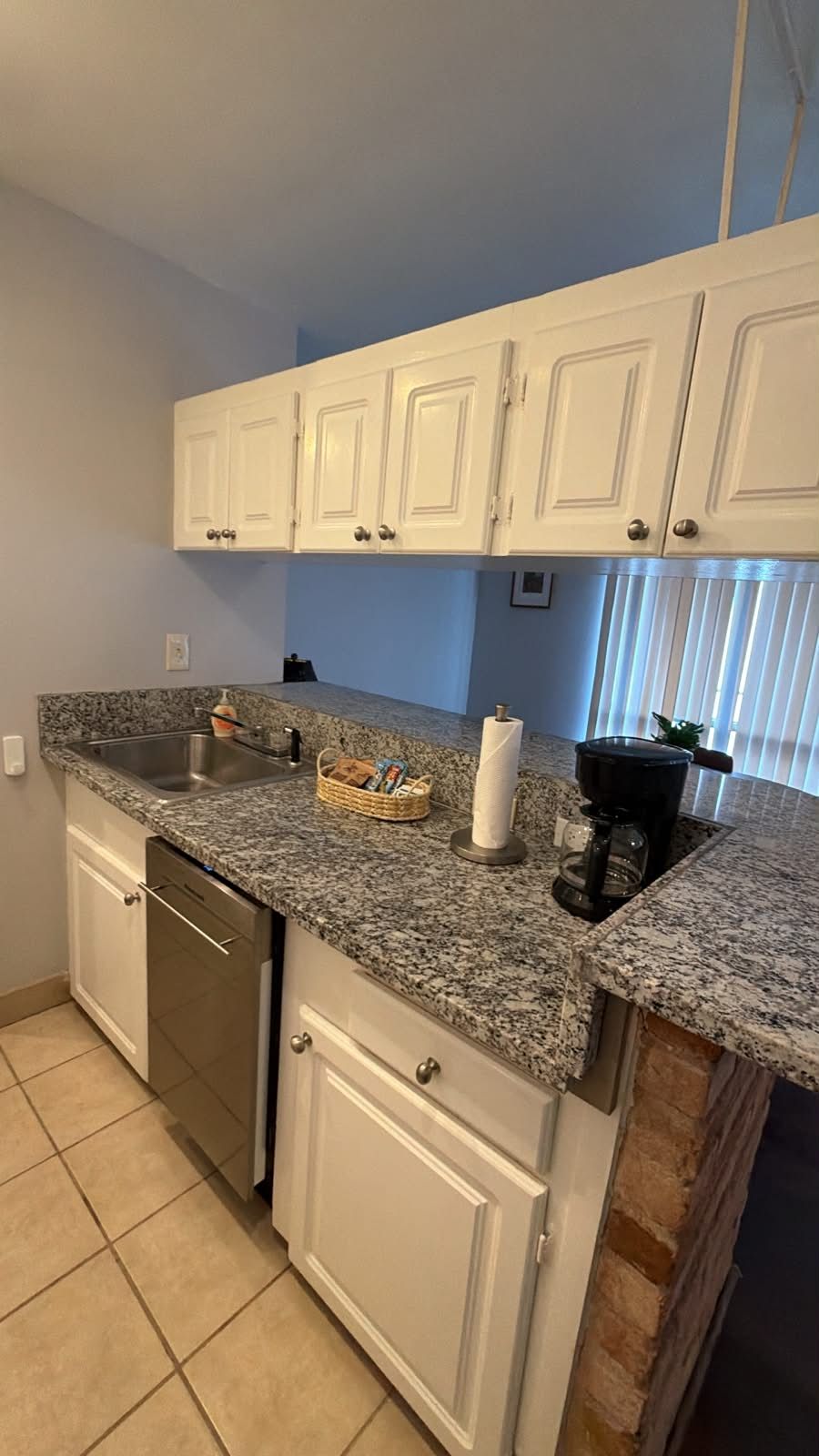 A kitchen with white cabinets, a granite countertop, a dishwasher, and a coffee maker.