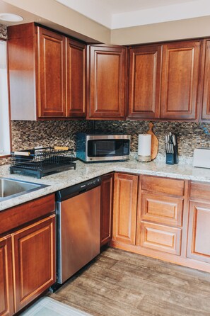 Una cocina con armarios de madera, un microondas de acero inoxidable, un lavavajillas y una encimera de granito.