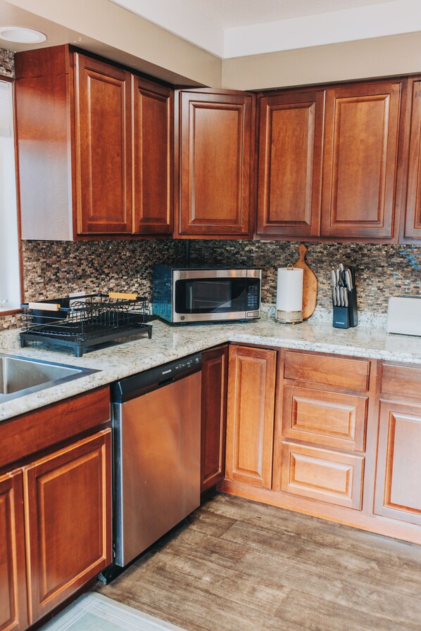 A kitchen with wooden cabinets, a stainless steel microwave, a dishwasher, and a granite countertop.