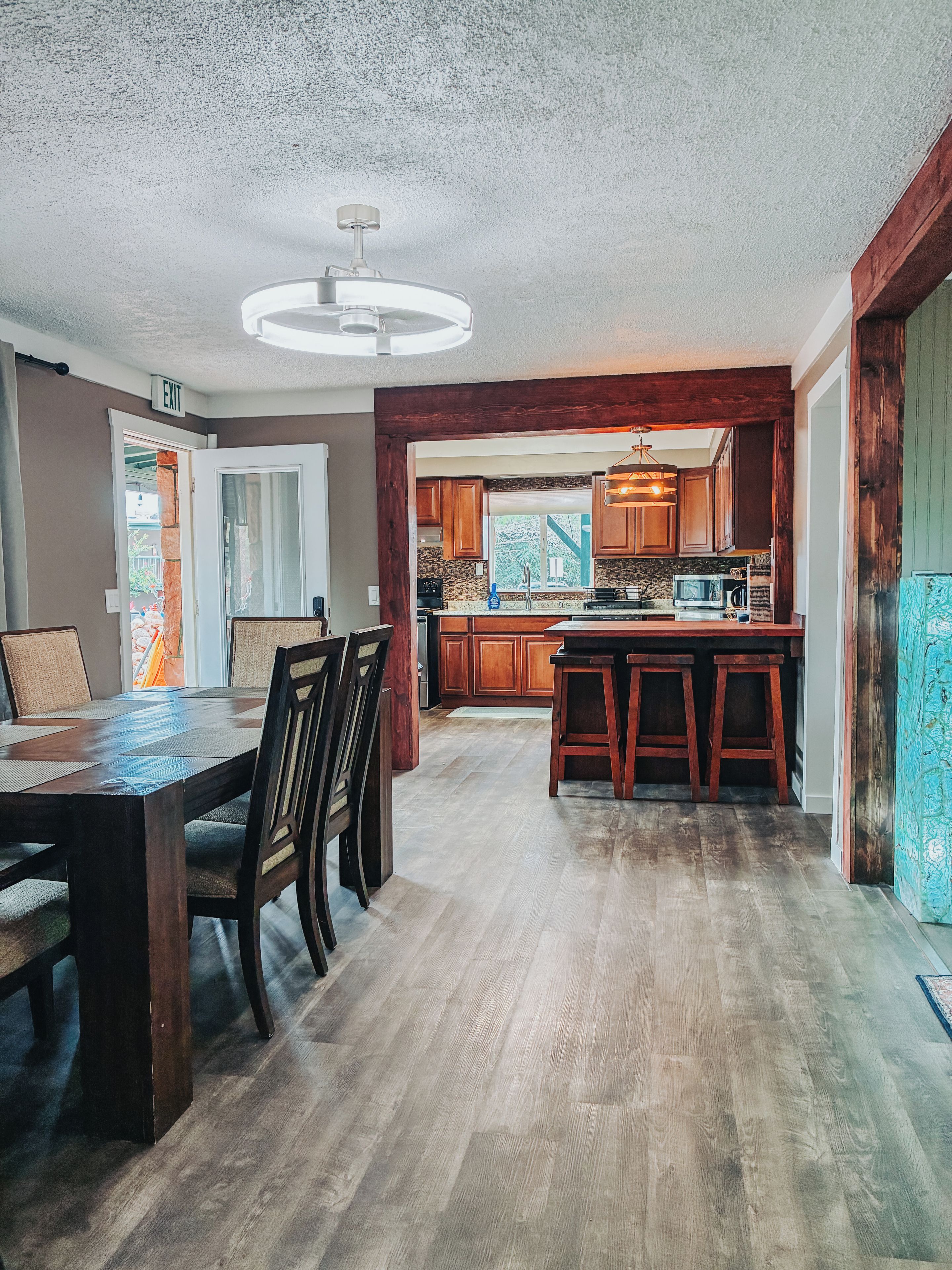 A spacious dining area with a wooden table and chairs, a kitchen with wooden cabinets and a built-in microwave, and a ceiling fan.