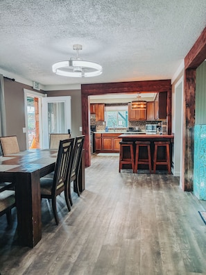 A spacious dining area with a wooden table and chairs, a kitchen with wooden cabinets and a built-in microwave, and a ceiling fan.