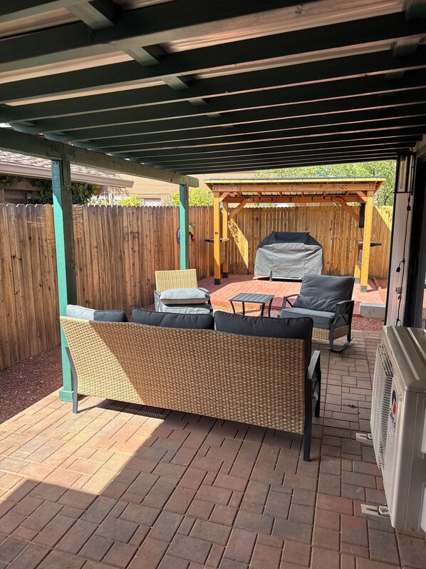 Un patio exterior con mobiliario de mimbre, una parrilla y una zona cubierta.