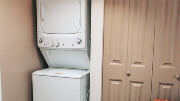 A laundry room with a washing machine and dryer, a wooden table, and a set of double doors.