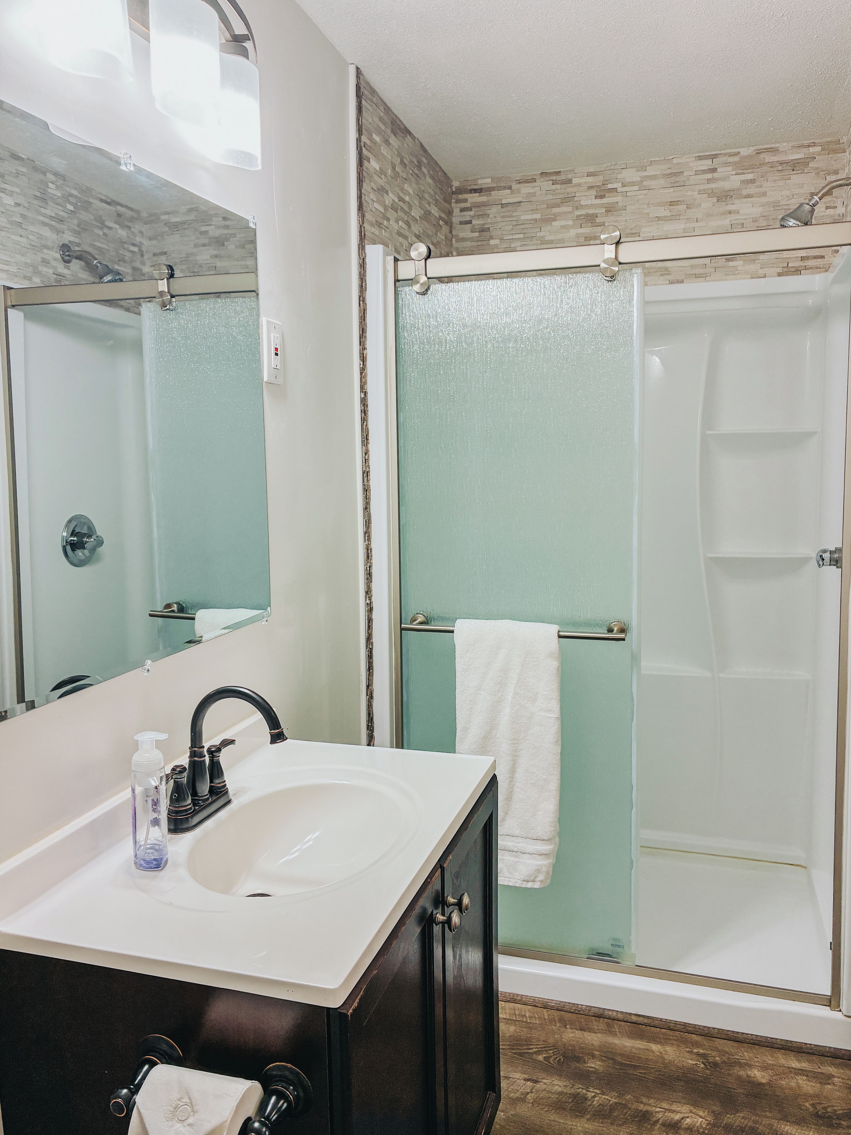 A bathroom with a white sink, dark cabinets, a glass shower enclosure, and a mirror.
