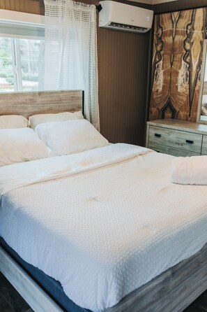 A neatly made bed with white linens, a wooden headboard, and a wall-mounted air conditioner.