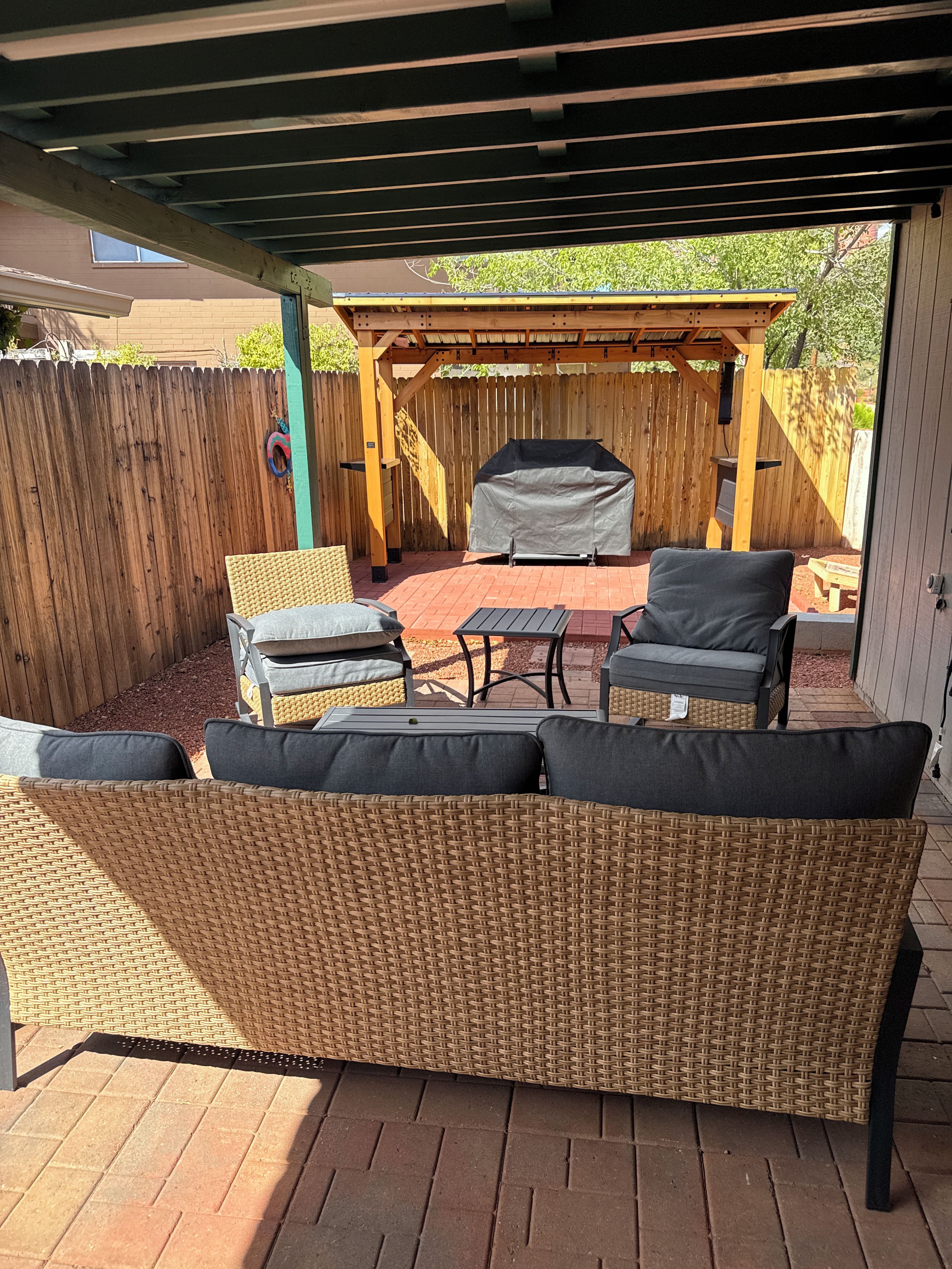 A covered patio area with a wicker sofa, a grill, and outdoor furniture.