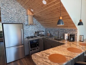 A modern kitchen with a stone backsplash, stainless steel appliances, and a wooden ceiling.