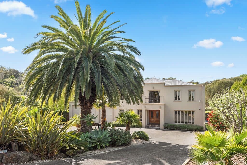 Un edifici de dues plantes amb una entrada i una palmera al primer pla.