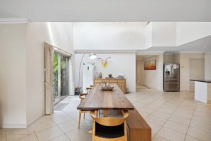 Una cocina moderna con una larga mesa de madera, electrodomésticos integrados y vistas al exterior.