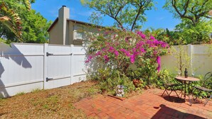 Un jardin avec une terrasse en briques, une clôture blanche et un arbre aux fleurs roses.