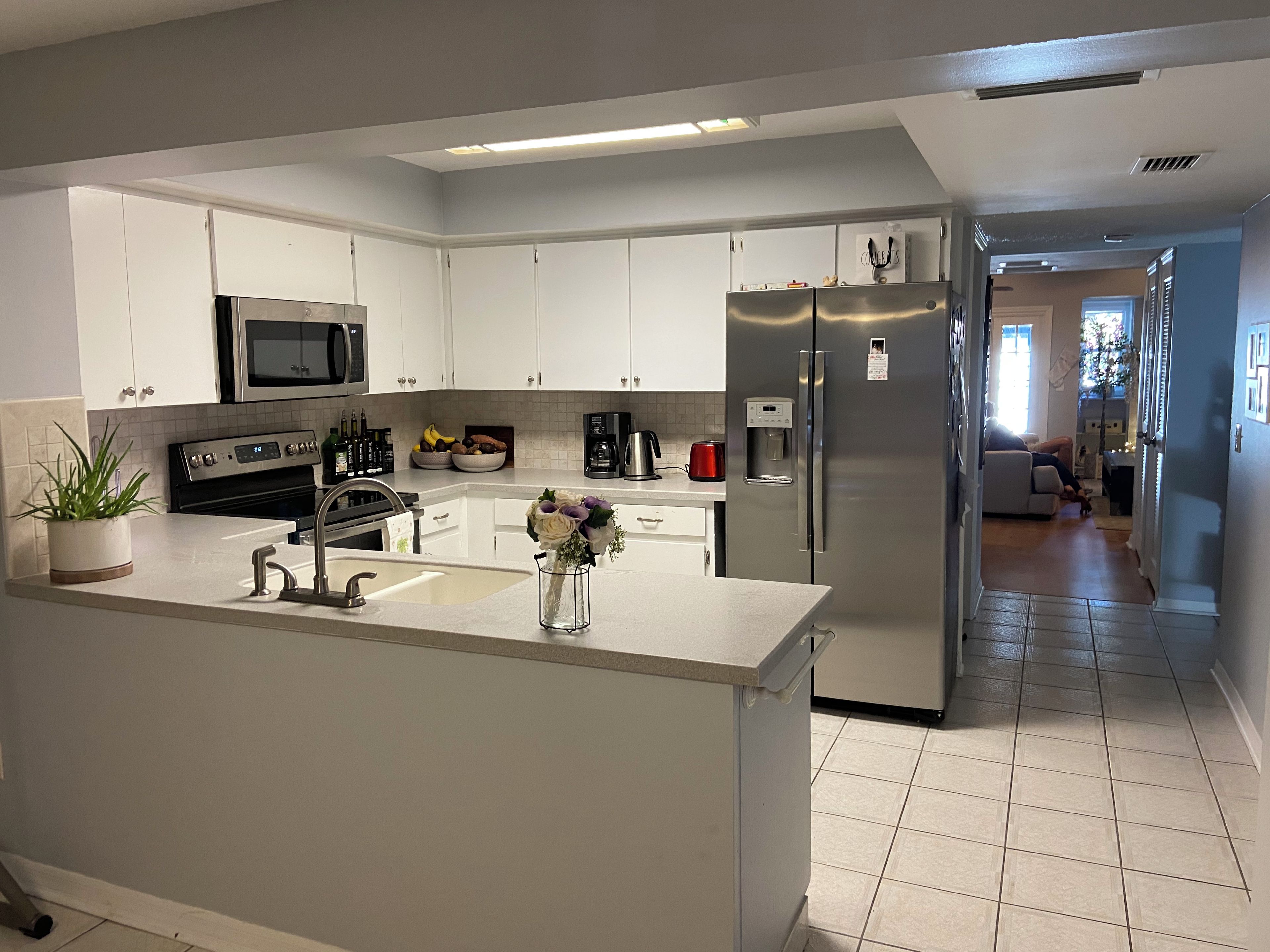 Een moderne keuken met witte kasten, roestvrijstalen apparatuur en een centraal eiland met een spoelbak en decoratieve vaas.