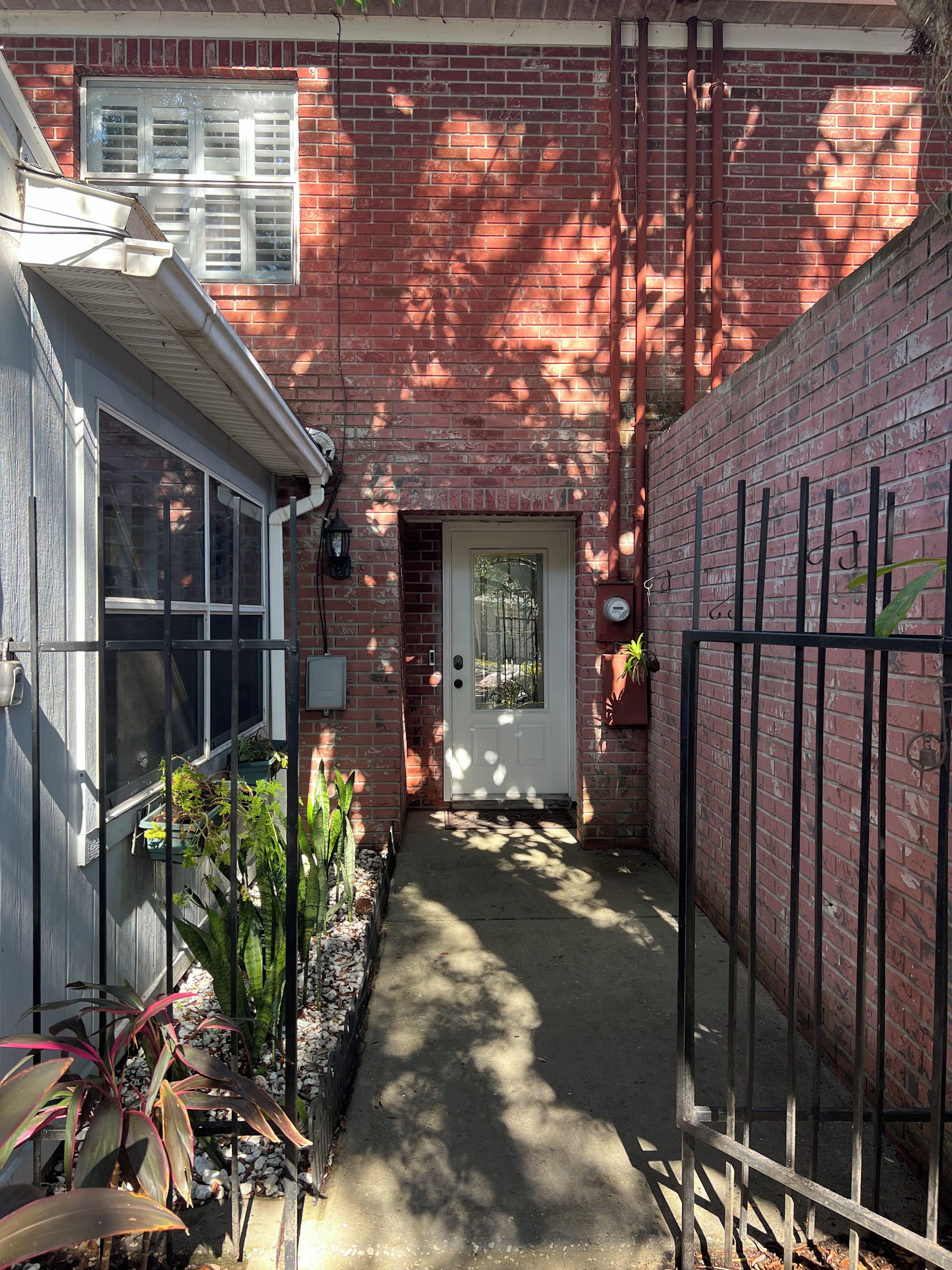 Une ruelle étroite, avec un mur de briques, une porte blanche et un portail en métal.