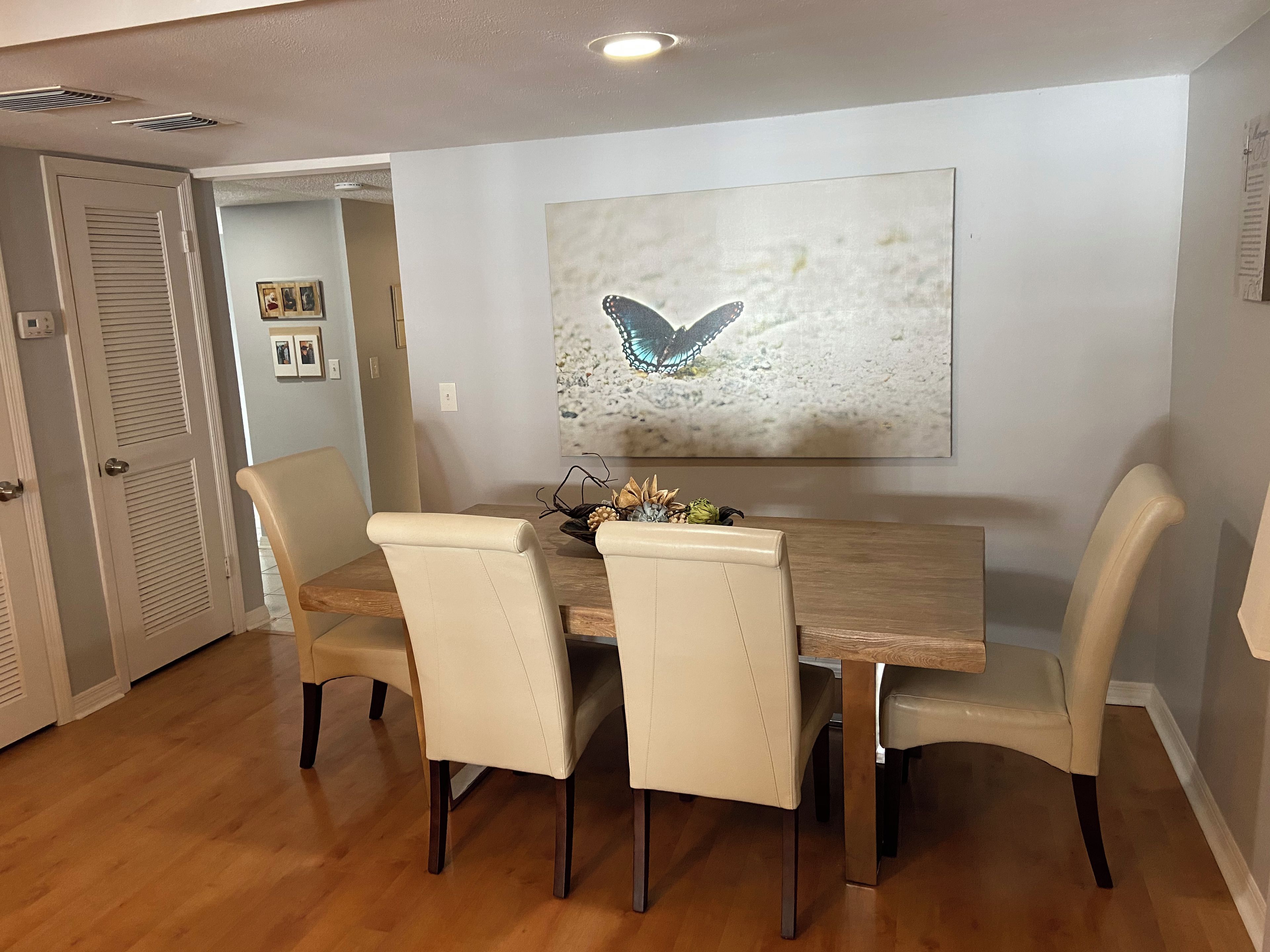A dining area with a wooden table, four chairs, and a butterfly artwork on the wall.