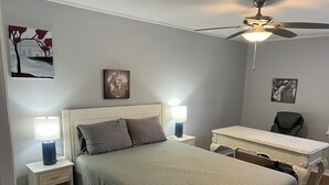 Une chambre à coucher comprenant un lit, deux tables de chevet avec des lampes, un bureau, une chaise et un ventilateur de plafond.