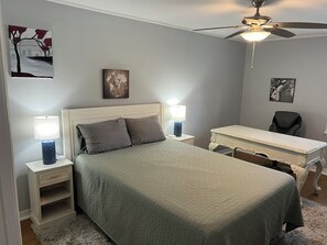 Un dormitorio con una cama, dos mesitas de noche con lámparas, un escritorio, una silla y un ventilador de techo.