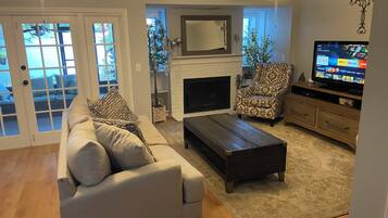 A living room with a sofa, armchair, coffee table, fireplace, TV, and ceiling fans.