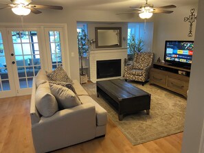 A living room with a sofa, armchair, coffee table, fireplace, TV, and ceiling fans.