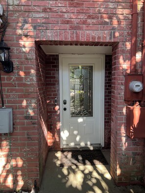 A red brick wall with a white door featuring a glass panel and a metal doorbell.