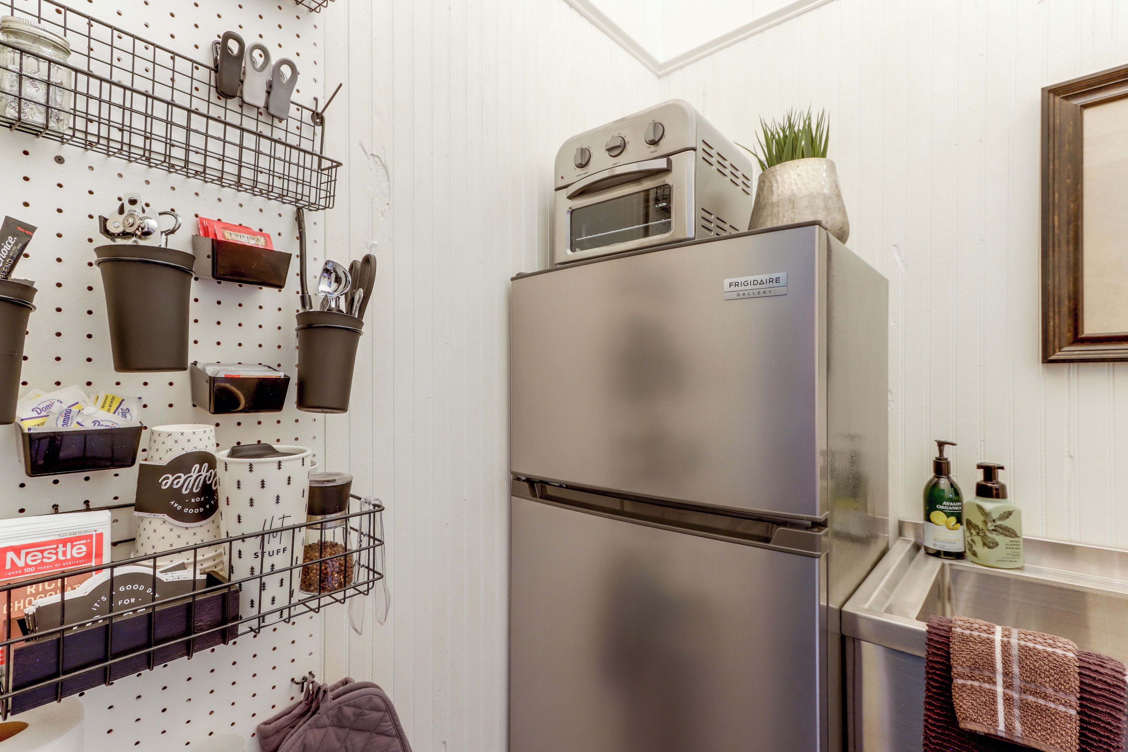 A kitchen with a stainless steel refrigerator, a pegboard with kitchen utensils, and a window above the sink.
