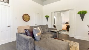 A living room with a gray sofa, a clock, and a mirror. - Walk Everywhere! Downtown Fort Smith Duplex (Fort Smith)