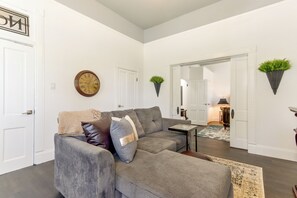 A living room with a gray sofa, a clock, and a mirror. - Walk Everywhere! Downtown Fort Smith Duplex (Fort Smith)