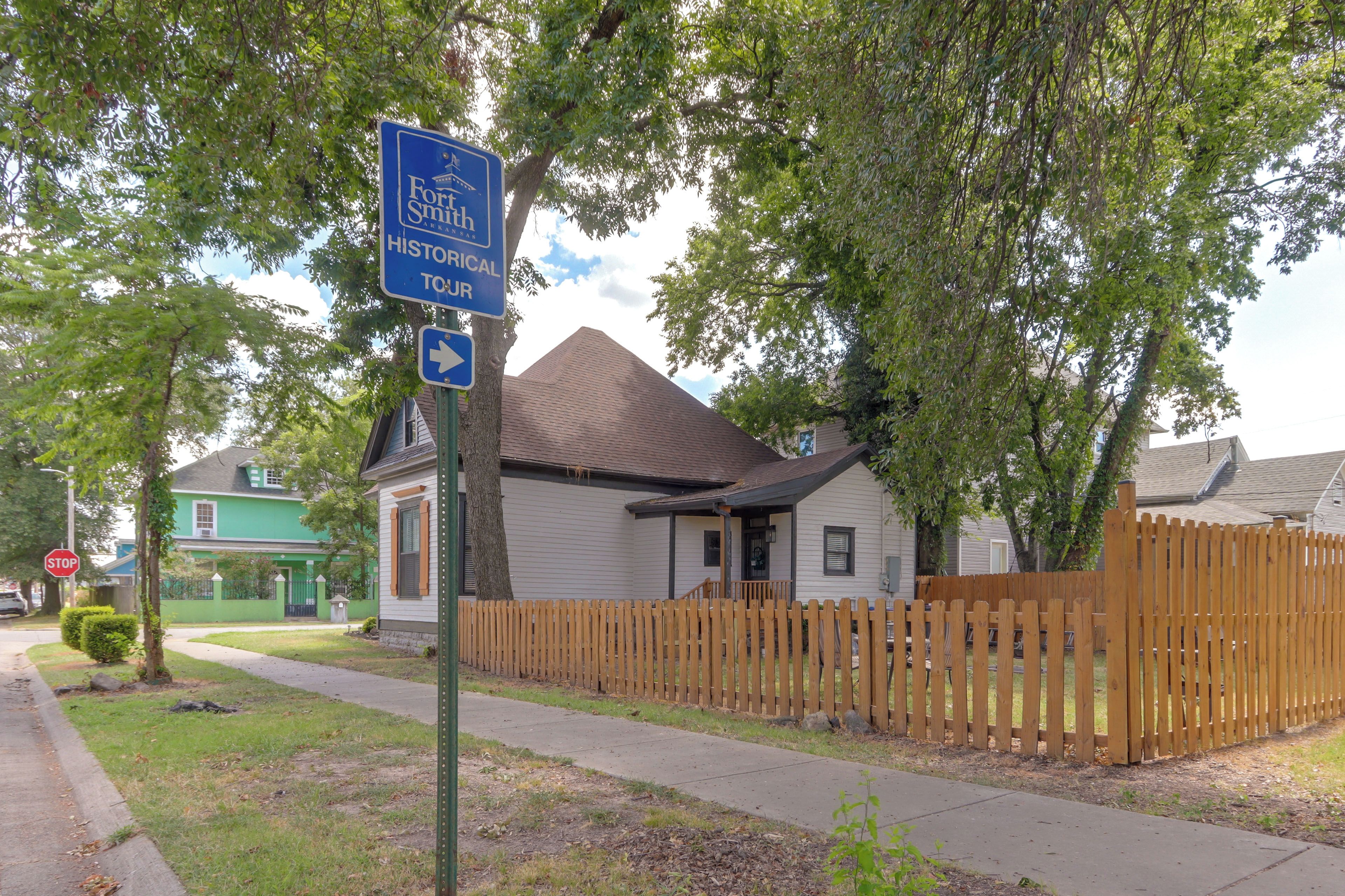 Un quartier résidentiel avec un panneau bleu indiquant un circuit touristique historique, un panneau de signalisation indiquant un arrêt obligatoire et des maisons entourées d’une clôture en bois.
