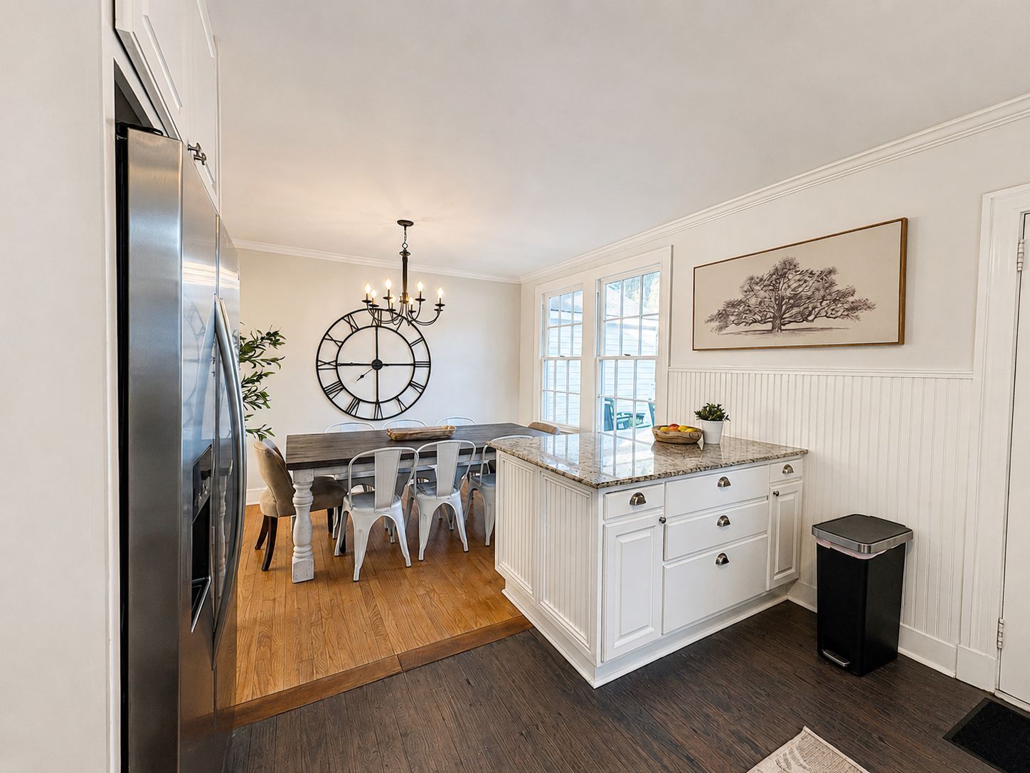 A kitchen with a central island, white cabinetry, a clock on the wall, and a trash can.
