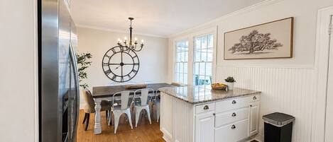 A kitchen with a central island, white cabinetry, a clock on the wall, and a trash can.