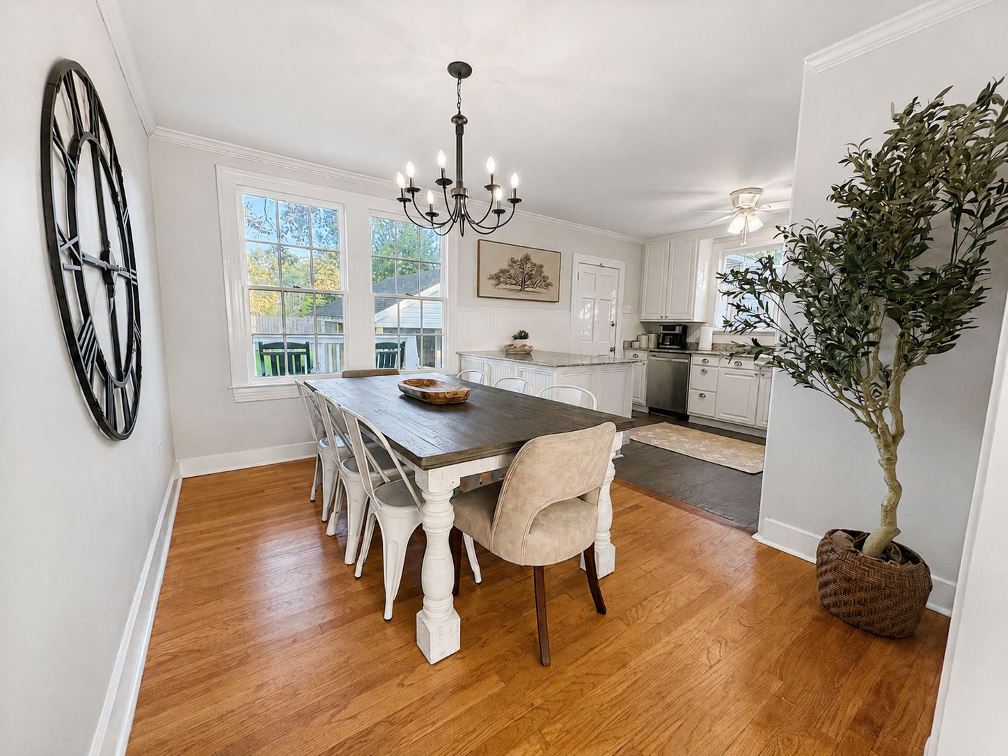 A dining area with a wooden table, white chairs, a chandelier, and a potted plant.