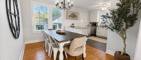 A dining area with a wooden table, white chairs, a chandelier, and a potted plant.