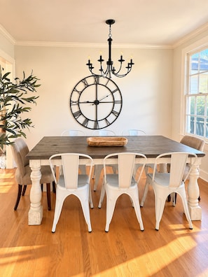 A dining room with a wooden table, white chairs, a wall clock, and a chandelier. - LSU Gameday Cottage - Sleeps 12 - Private Gated Patio/Deck/Firepit (Baton Rouge)