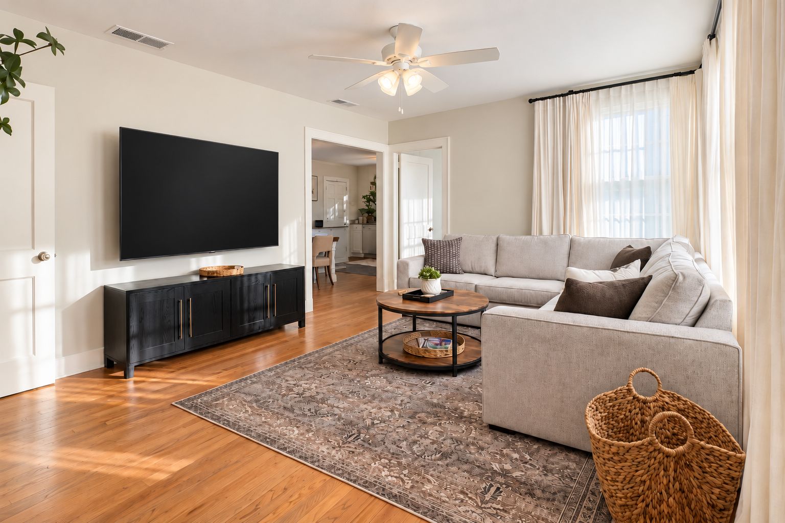 A modern living room with a flat-screen TV, a grey sofa, a coffee table, and a patterned rug.