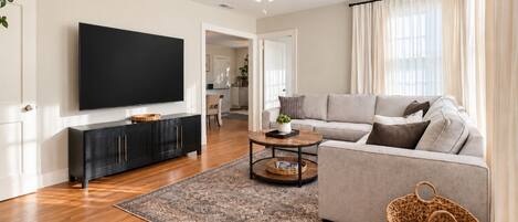A modern living room with a flat-screen TV, a grey sofa, a coffee table, and a patterned rug.