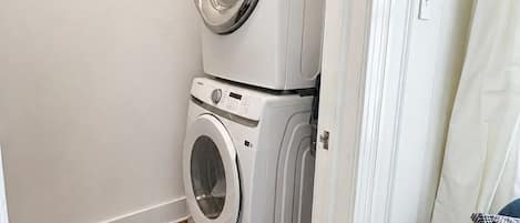 Un lavadero pequeño con dos lavadoras apiladas, suelo de madera y puerta blanca.
