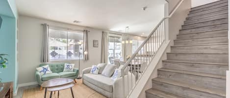 A living room with a staircase, a sofa, a coffee table, and a view of the outside.