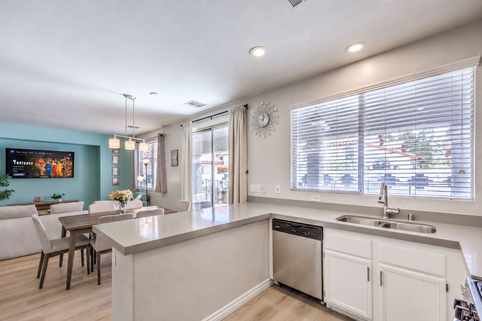 A modern kitchen with a central island, a dining area with a sofa and chairs, and a large window with blinds.