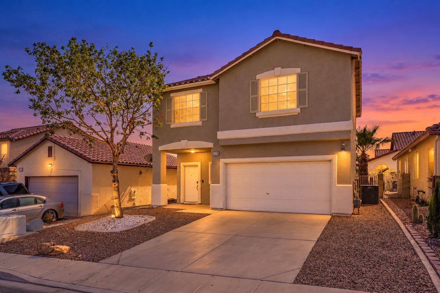 A two-story house with a garage, a driveway, and a tree in the front yard.