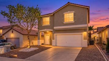 A two-story house with a garage, a driveway, and a tree in the front yard.