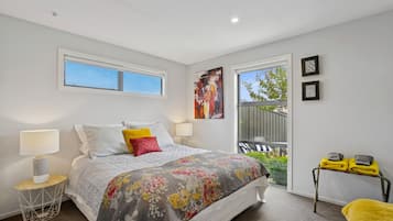 A bedroom with a bed, two bedside lamps, a window, and a balcony with chairs.
