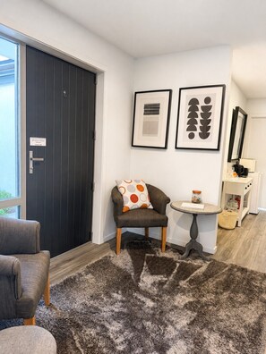 A modern room with a dark door, a grey armchair, a small round table, and two framed artworks on the wall.