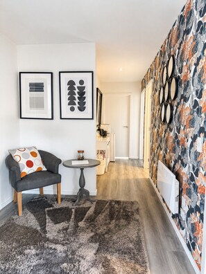 Una sala de estar moderna con un sofá gris, una mesa redonda y un tapete estampado. Hay obras de arte enmarcadas en la pared y un espejo decorativo.