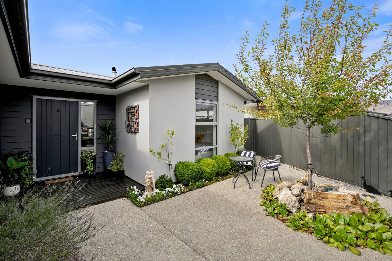 A modern house with a patio, a small garden, and a tree.